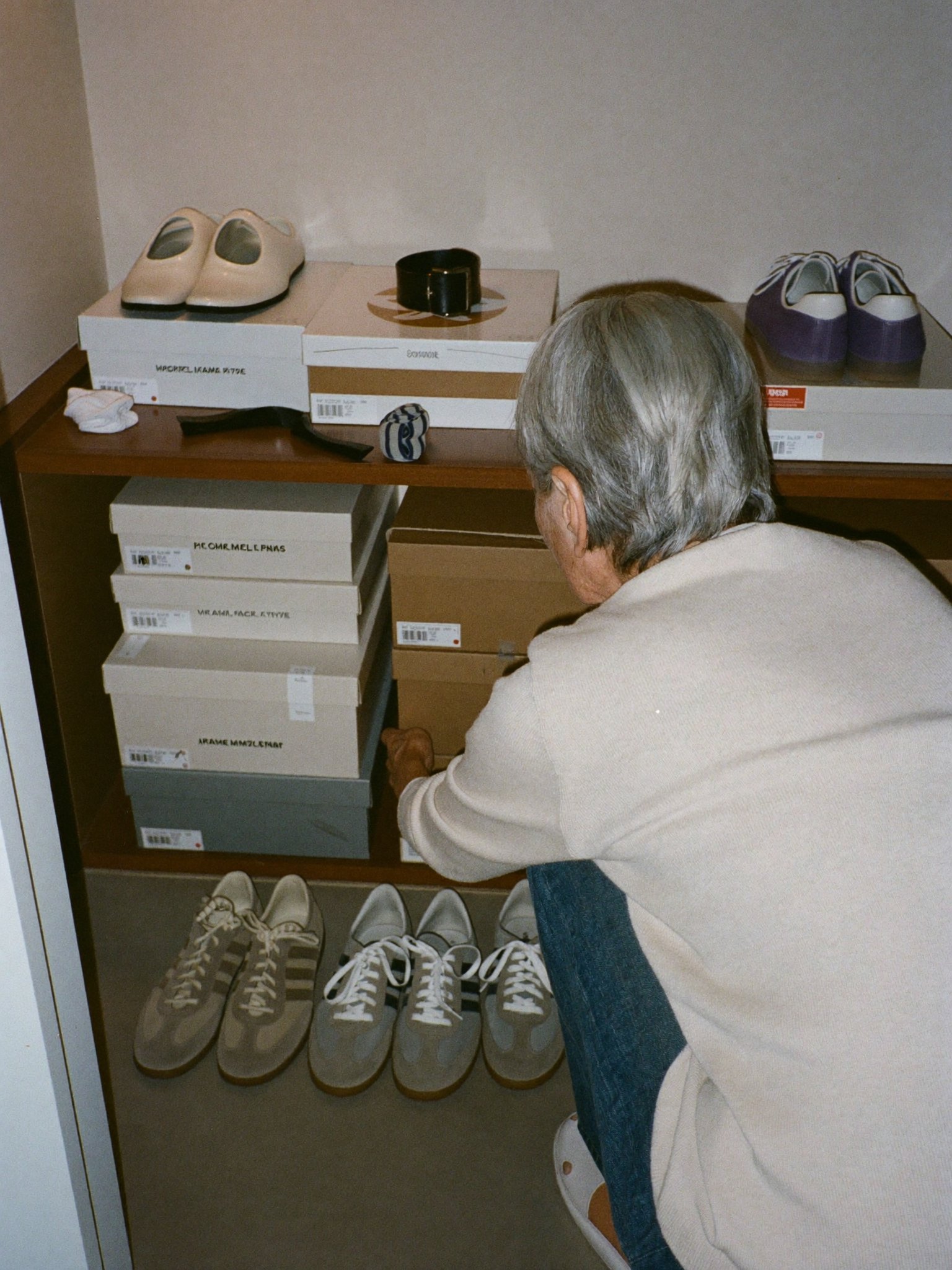 A woman kneeling in front of a closet shelf stacked with shoe boxes