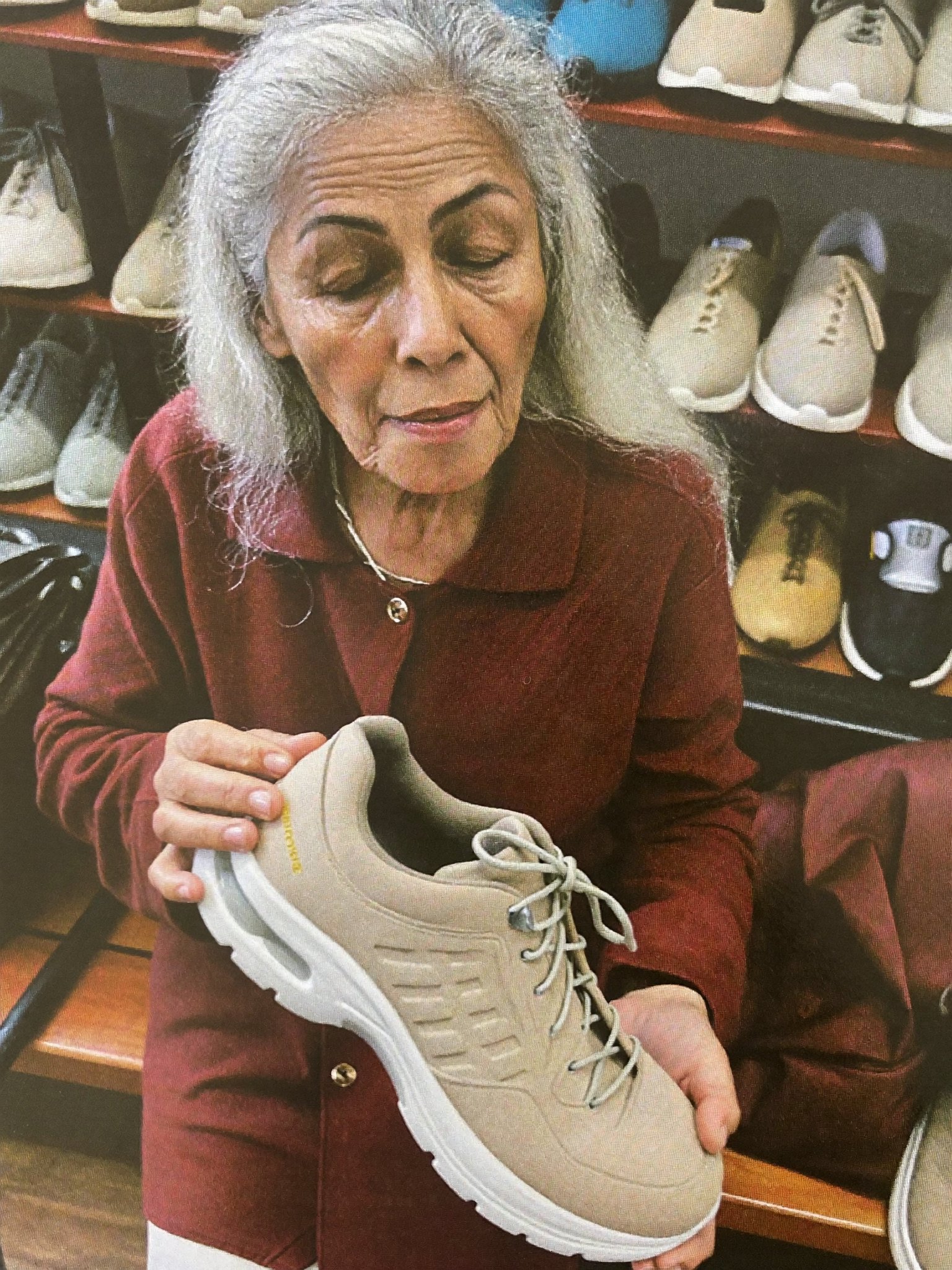 A woman in a shoe store holding up a bulky beige orthopedic walking shoe with a doubtful look