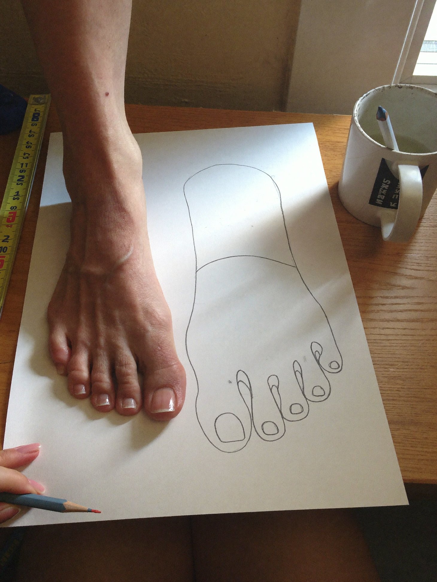 A bare foot standing on a sheet of paper next to its pencil outline, widest at the toes