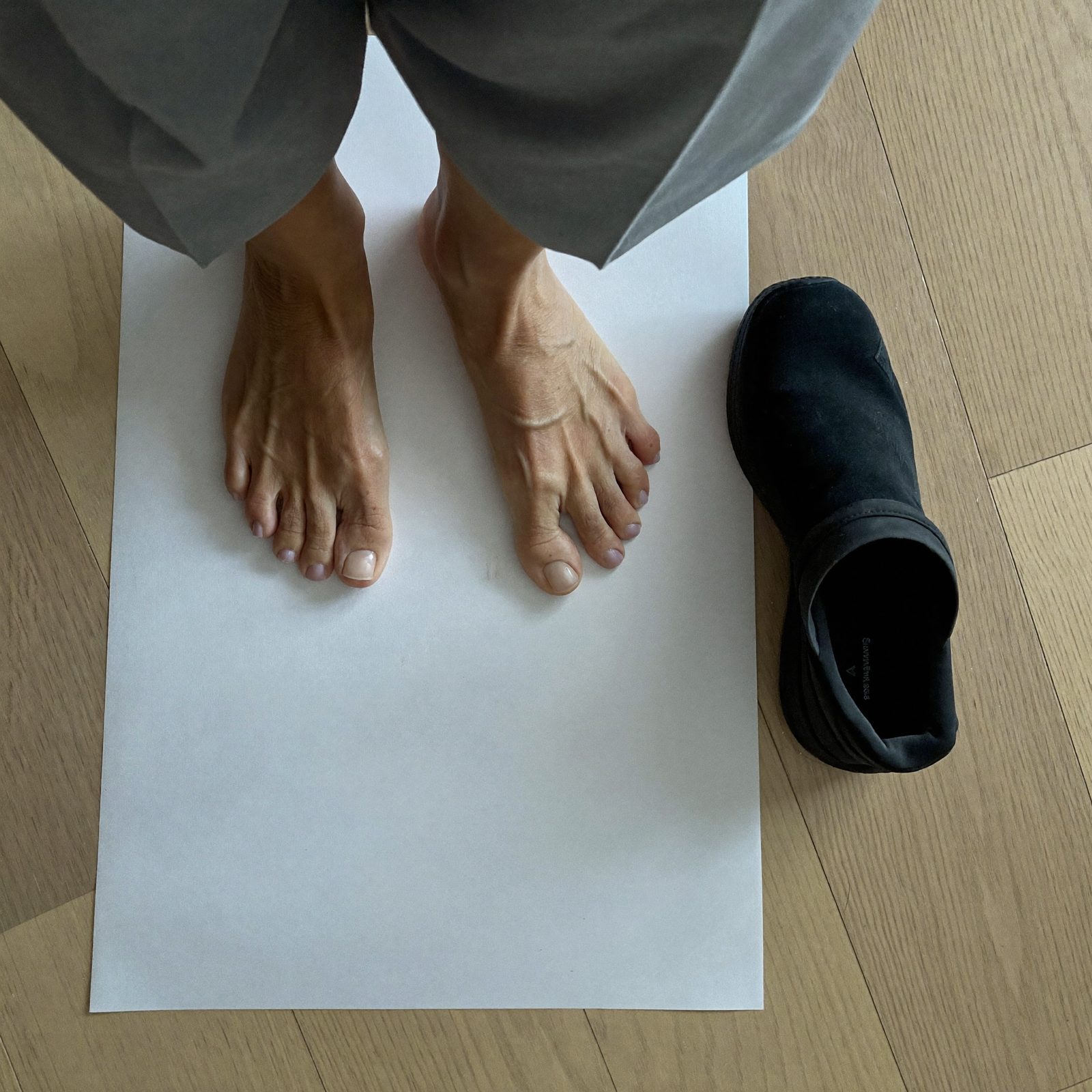 Overhead view of a woman's bare feet on a blank sheet of paper next to an Ample Daily shoe, showing the shoe is as wide as her toes