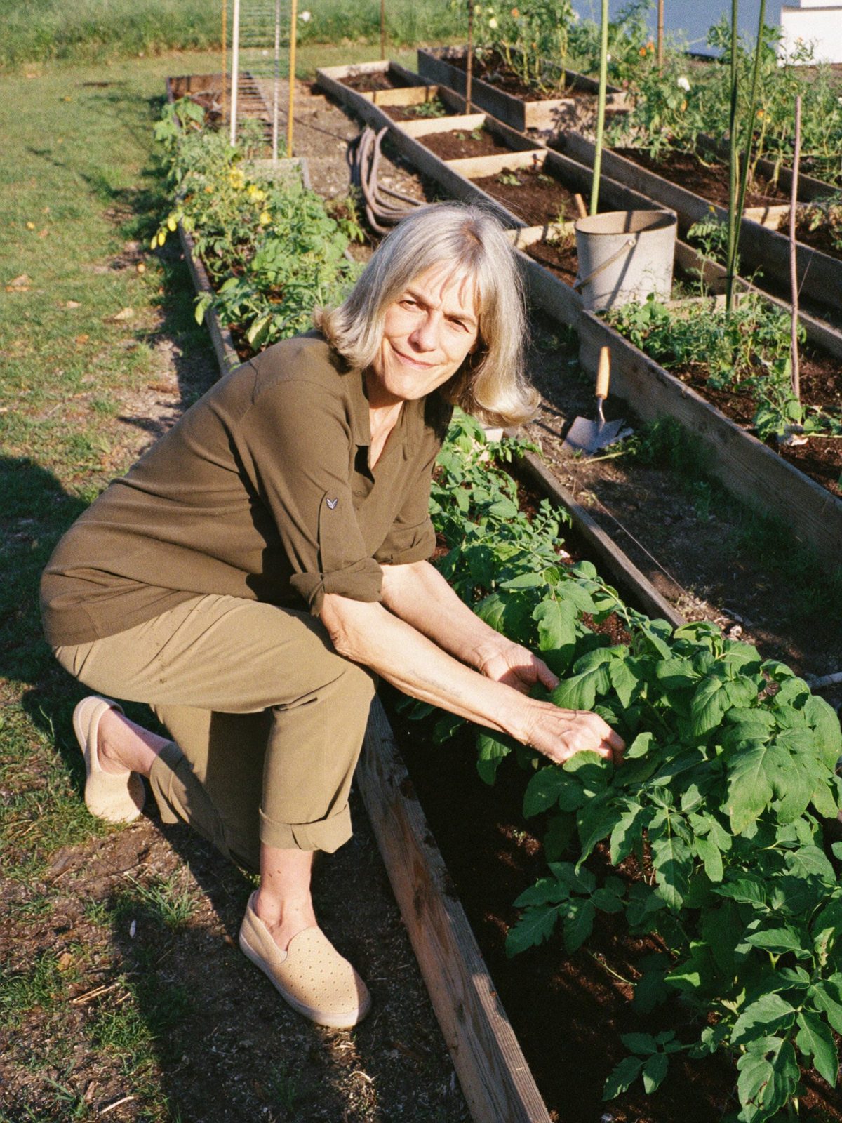 A woman in her sixties kneeling in a vegetable garden wearing sand-coloured Ample Daily sneakers