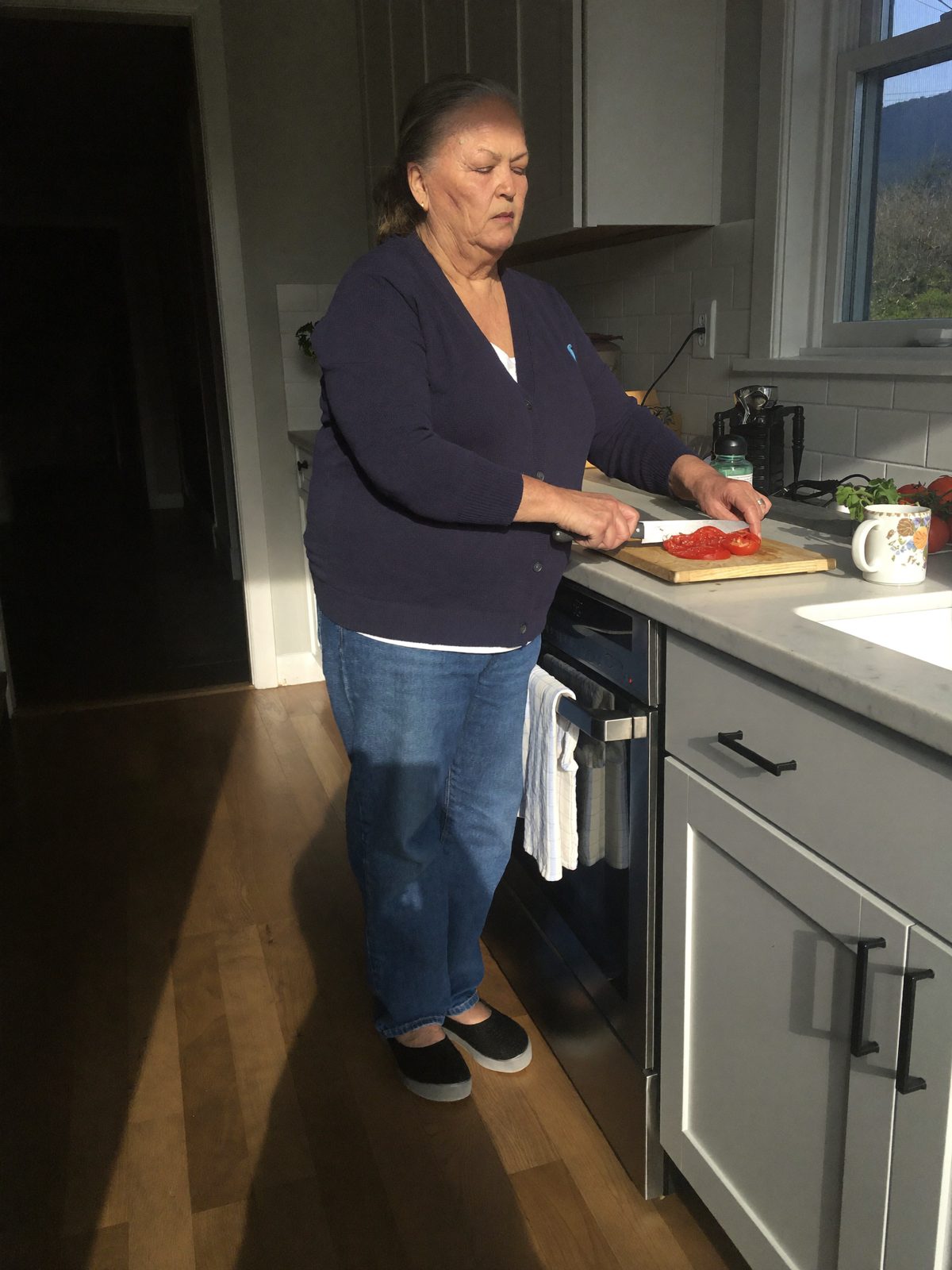 A woman in her sixties cooking at a kitchen counter wearing black Ample Daily sneakers