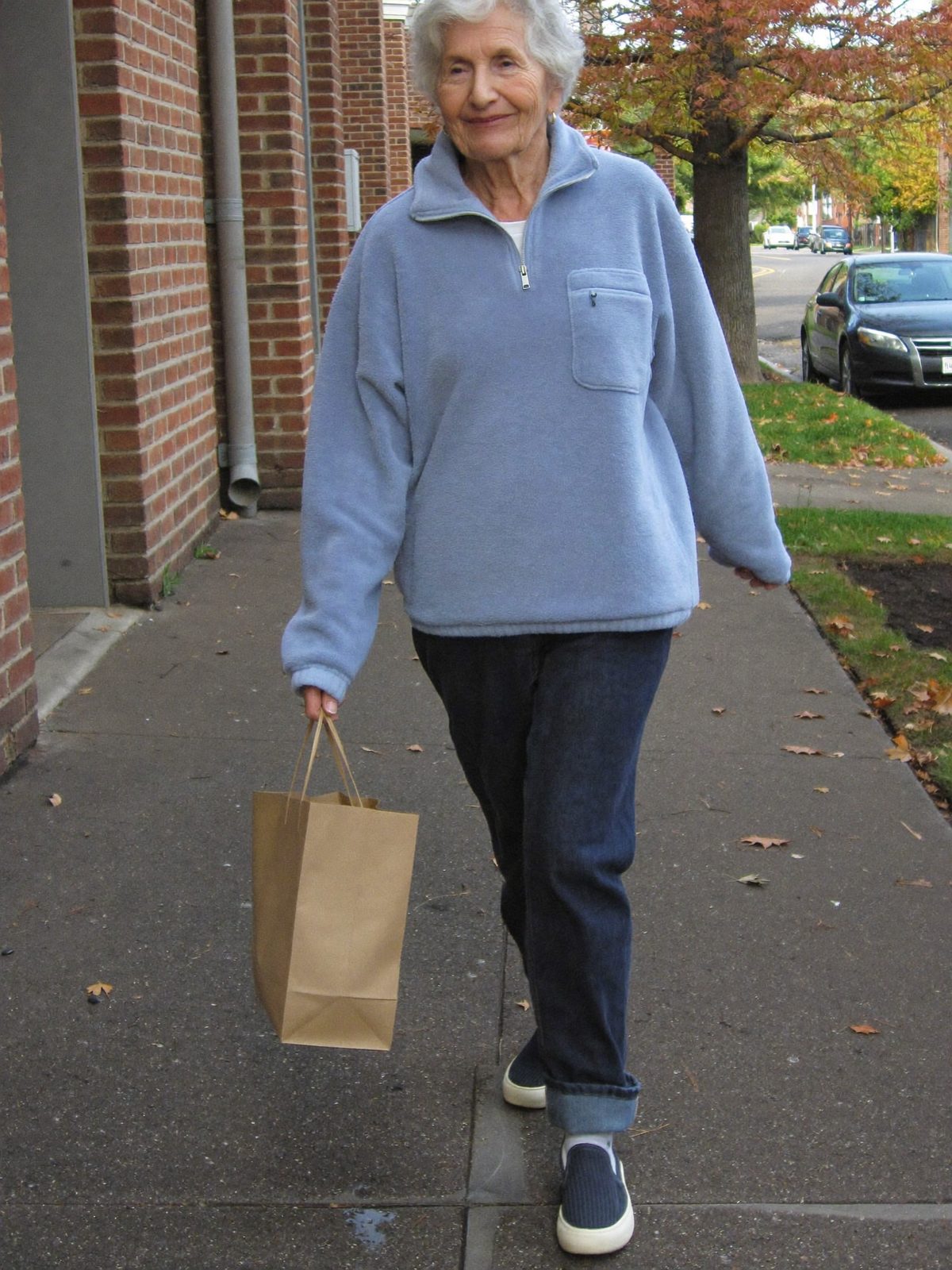 A woman in her sixties walking on a sidewalk carrying groceries wearing navy Ample Daily sneakers